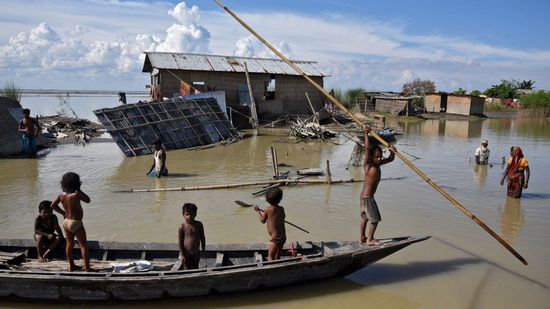 Children row a boat as they pass through damaged houses at a flood-affected village in Morigaon district